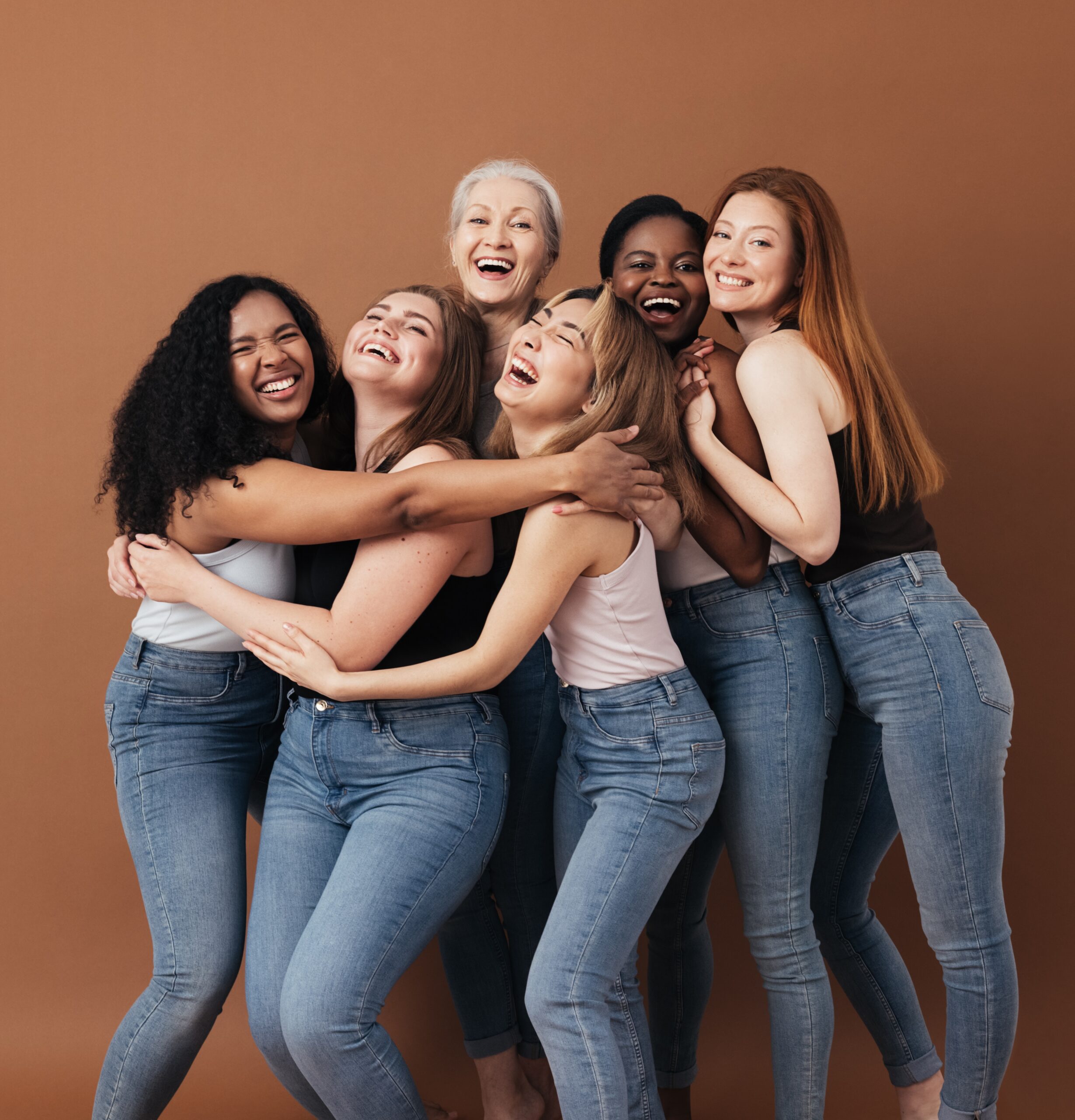 Six laughing women of a different race, age, and figure type. Group of multiracial females having fun against a brown background.